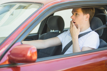 Junger Mann sitzt im Auto und ist schockiert