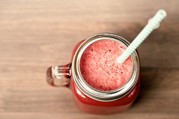 A watermelon smoothie in a mason jar with tube on wooden background. Sepia toning