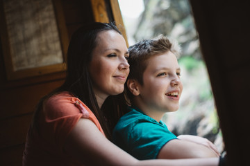 Young mother and her son enjoys traveling by old steam train. They looks through the open window and smiling. Photo was edited to match old film look.