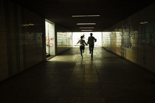 Young couple running hand in hand in a dark underpass, partial view