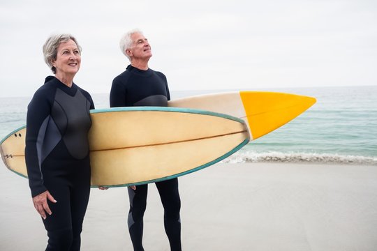 Senior couple with surfboard standing on the beach
