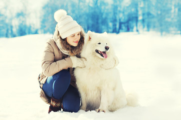 Woman owner hugging white Samoyed dog in winter park