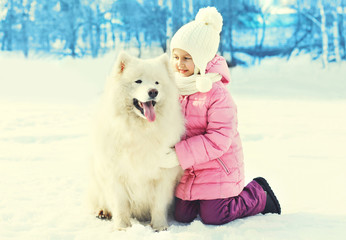 Little child with white Samoyed dog together on snow in winter p