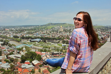 Fototapeta na wymiar Girl smiling and looking panoramic view of Tbilisi, Georgia. Girl-tourist walks around the city by looking at the view from above