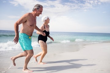Senior couple holding hands and running on beach