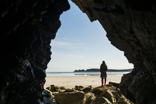 France, Bretagne, Finistere, Crozon peninsula, woman standing on the beach as seen from rock cave
