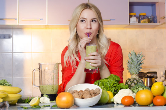 Cute girl drinking smoothie in kitchen and looking up, healthy lifestyle concept. Fruit on kitchen counter
