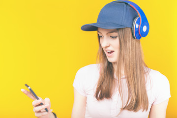 Surprised teenage girl uses a headphones and mobile phone