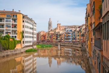 Fototapeta na wymiar Colorful yellow and orange houses and bridge Pont de Sant Agusti reflected in water river Onyar, in Girona, Catalonia, Spain. Church of Sant Feliu and Saint Mary Cathedral at background.