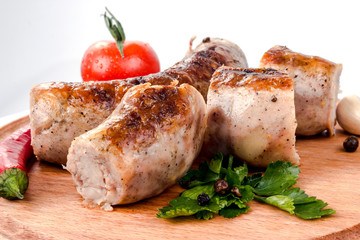 fried pork sausages on a barbecue on a wooden plate with cherry tomatoes and hot peppers