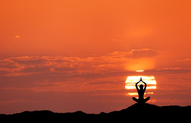 Sunset landscape with girl practicing yoga on the background of sun and red sky in the hill in summer