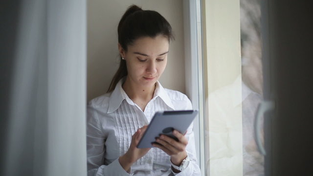 Woman at a window scrolling through her tablet