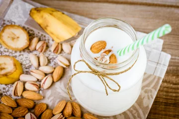 Foto auf Acrylglas Milchshake Banana and almond milk smoothie in a jar and mixed nuts on a rustic table
