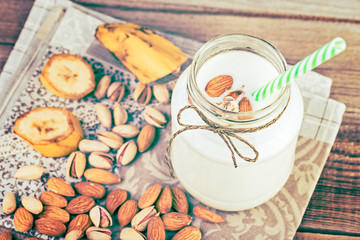 Banana and almond milk smoothie in a jar and mixed nuts on a rustic table