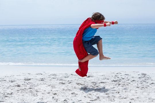 Boy in superhero costume jumping at sea shore