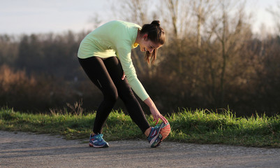 Young female runner doing exercise in evening sun