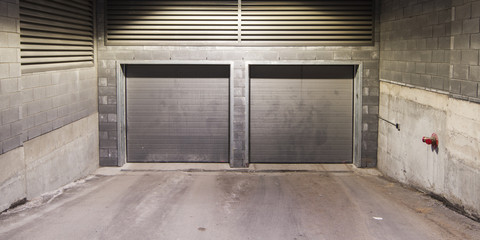Two metal garage doors with a brick wall
