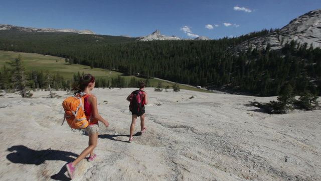Hiking people - hikers couple in Yosemite walking on hike wearing backpacks. Happy sporty couple walking down from the Pothole Dome, Yosemite National Park, California, USA.