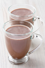 Hot cocoa beverage / Hot cocoa beverage in transparent glass mug on wooden background              