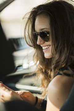 Portrait of smiling teenage girl with sunglasses sitting in a car using her smartphone