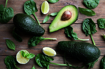 Sliced avocado with fresh spinach, basil and lime on wooden background, close up