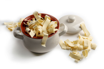 Dry pasta in a ceramic pot isolated on white, close up