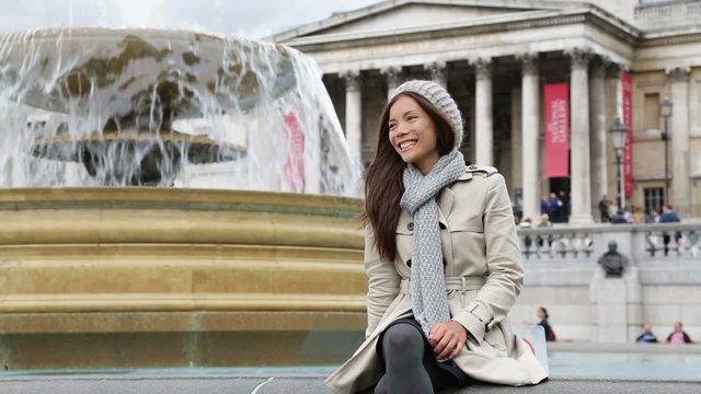 London woman on Trafalgar Square smiling happy laughing having fun sitting and relaxing. Beautiful multiracial Asian Caucasian girl tourist on travel vacation in London, England, United Kingdom