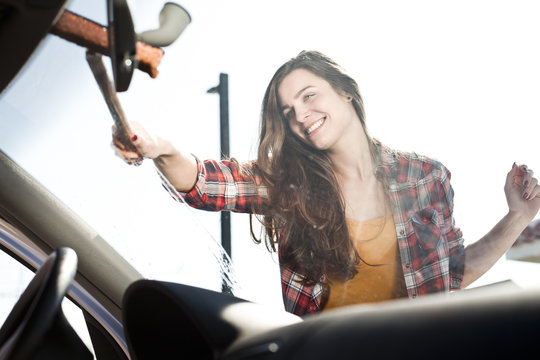 Smiling young woman cleaning windshield of a car