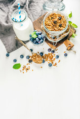 Healthy breakfast ingrediens. Homemade granola in open glass jar, milk or yogurt bottle, blueberries and mint