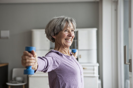 Portrait of happy senior woman doing fitness exercise with dumbbells at home