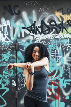 Portrait of smiling young woman standing in front of graffiti wall