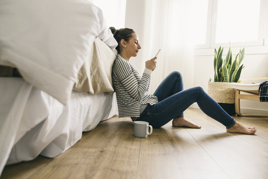 Relaxed woman sitting in bedroom looking at cell phone