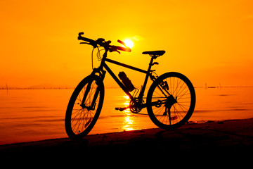 Fototapeta na wymiar Silhouette of bicycle on the beach against colorful sunset in the sea. Outdoors.