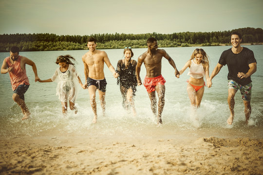 Germany, Haltern, seven friends running hand in hand out of Lake Silbersee having fun