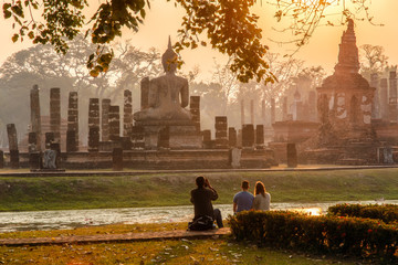 Fototapeta premium Japanese Man take a photo european traveller in sunrise time at Sukhothai historical park, the old town of Thailand in 800 years ago