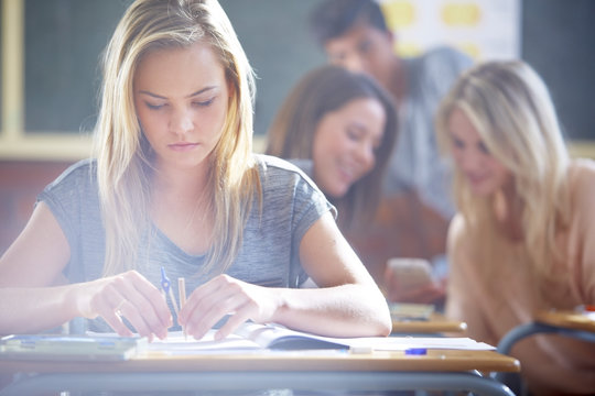 Female student in classroom using compasses at desk