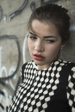 Portrait of sad young woman with red lips in front of wall with graffiti