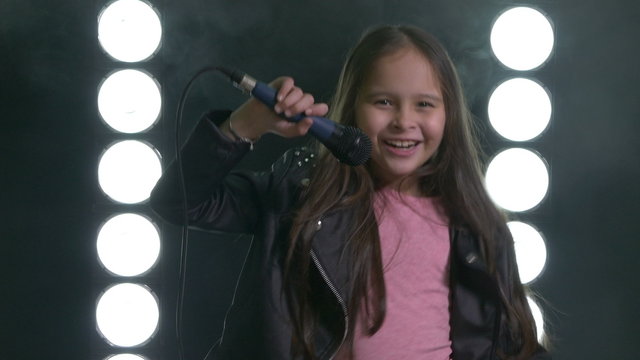 Young Asian American girl dancing with microphone with smoke and stagelight in background.