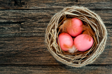 Easter pink eggs in nest on rustic wooden background