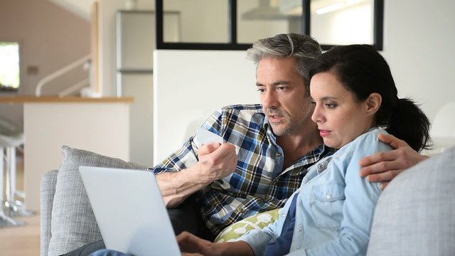 Couple in sofa websurfing and shopping on internet