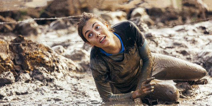 Participant in extreme obstacle race crawling under barbed wire