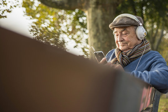 Senior man on park bench with cell phone and headphones