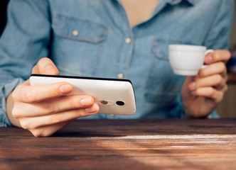 Woman in a denim shirt reading news on mobile phone and drinking
