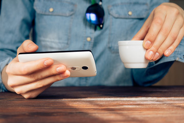 Woman in a cafe holding a cell phone and drinking coffee
