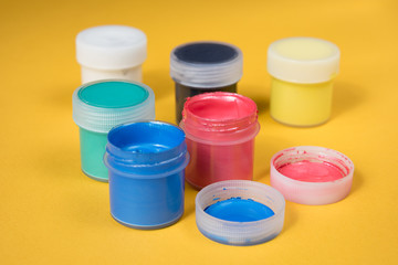Opened bottles of watercolor paint on a yellow paper