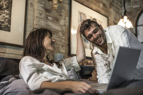 Happy couple together in bed looking at laptop