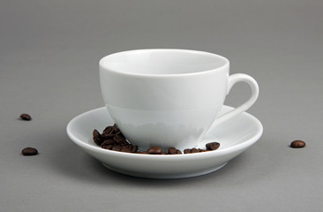 Coffee beans spilling out from a coffee cup on gray background.