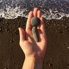Woman hand holding small stones in hand near blue sea on a beach background