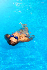 Young woman floating in a swimming pool , looking at the sky.