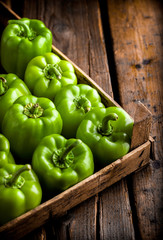 Green peppers in rustic wooden box overhead on wooden table and dark background in studio
